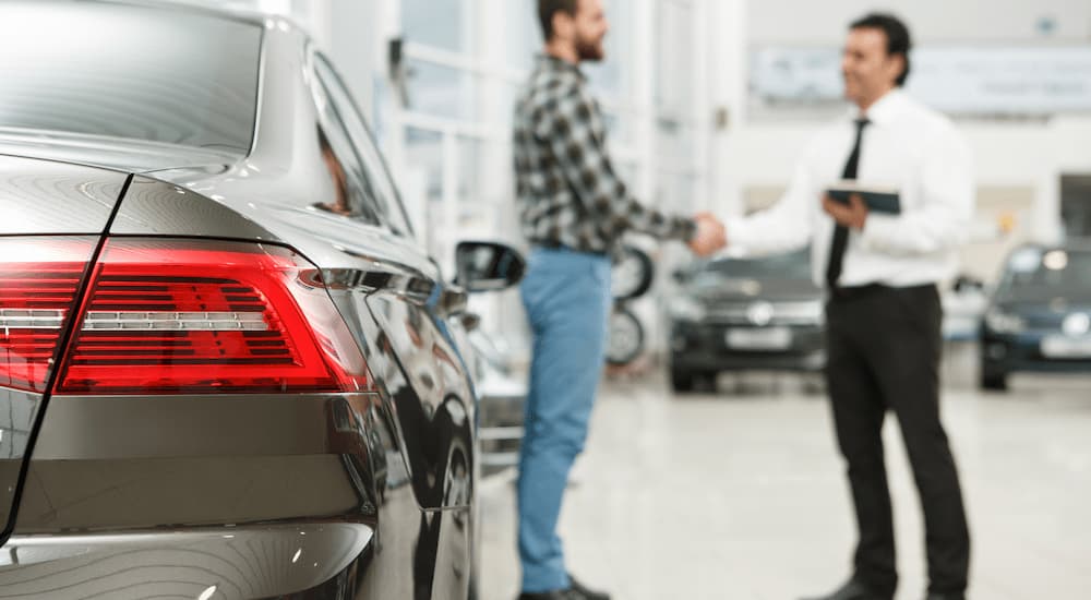 A car salesman is shown shaking hands with a customer in the middle of a short-term car rental place.
