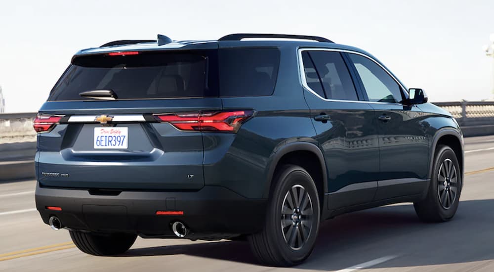 A blue 2023 Chevy Traverse is shown from the rear driving on an open road.