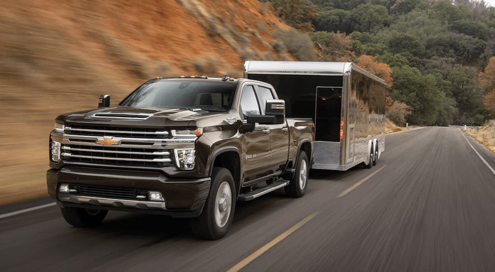 A brown 2023 Chevy Silverado 2500 HD is shown towing an enclosed trailer on an open road.