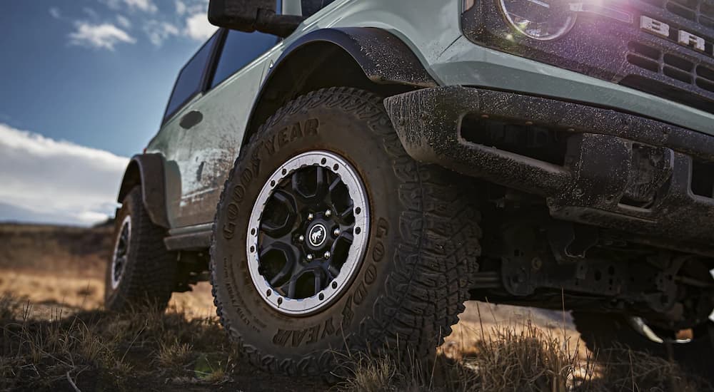 A close up of the tire on a light blue 2023 Ford Bronco Black Diamond is shown in an open field.