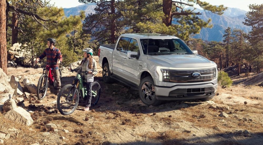 A silver 2023 Ford F-150 Lightning is shown parked next to people biking.