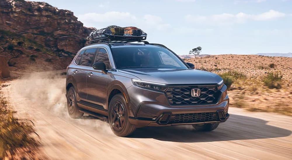 A dark grey 2023 Honda CR-V Sport Hybrid is shown driving on a dusty trail.