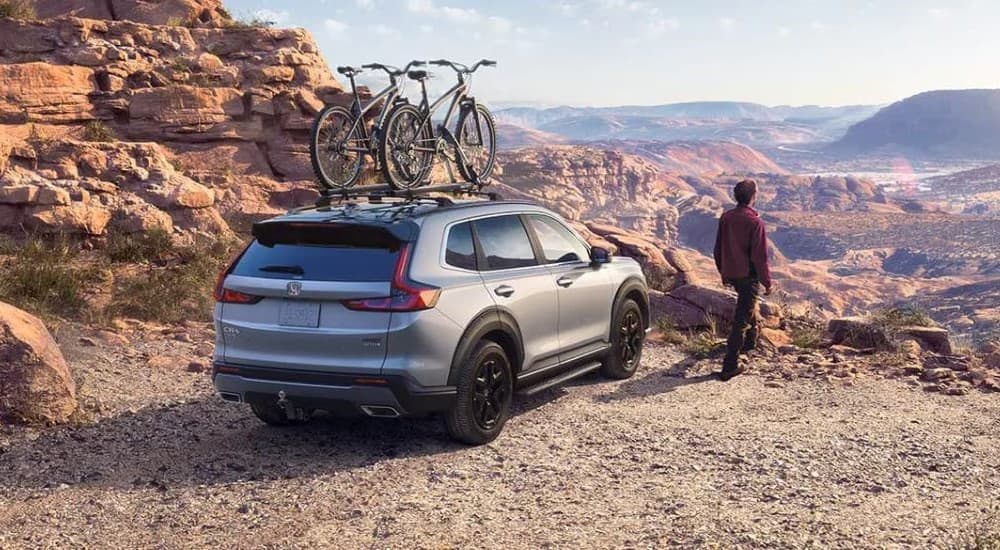 A silver 2023 Honda CR-V Sport Touring Hybrid is shown overlooking rock formations.