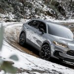 A silver 2023 Honda HR-V is shown driving on a muddy and snow-covered road.