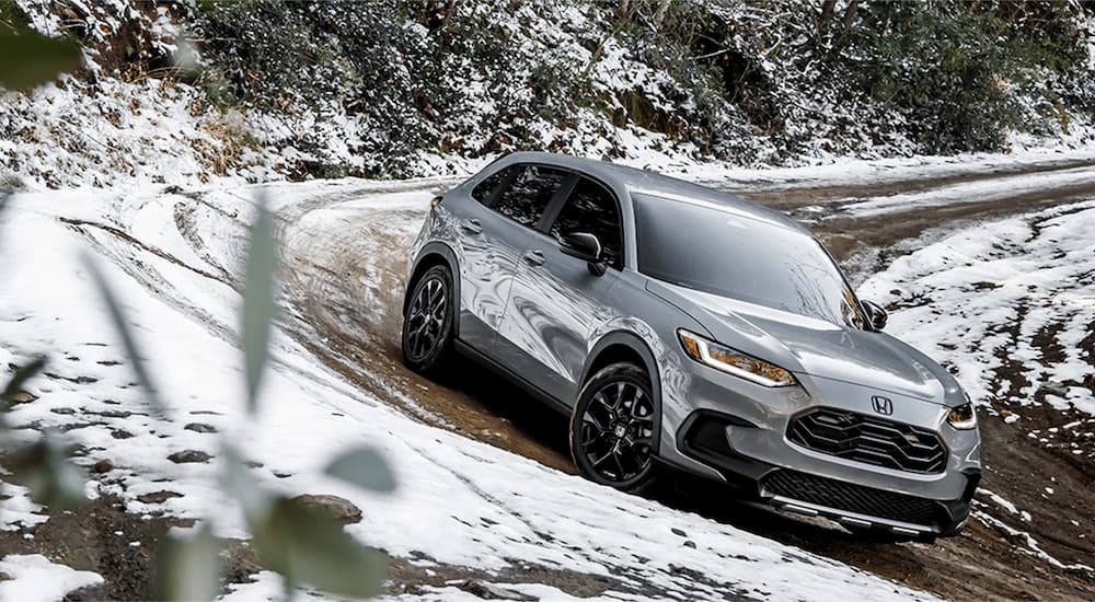 A silver 2023 Honda HR-V is shown driving on a muddy and snow-covered road.