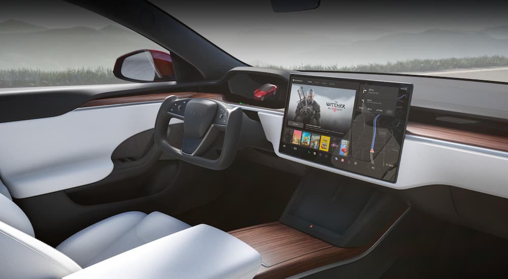 The grey and black interior of a 2023 Tesla Model S shows the steering wheel and infotainment screen.