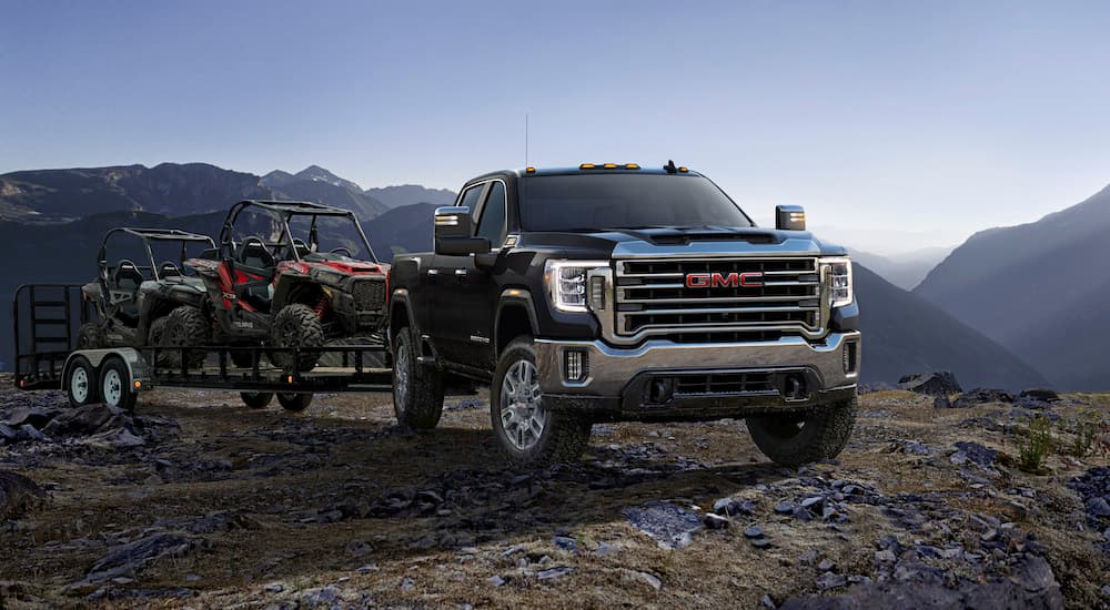A black 2023 GMC Sierra 2500HD is shown from the front while towing a pair of UTVs.