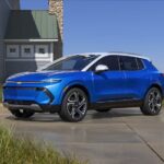 One of the most popular electric vehicles for sale, a blue 2024 Chevy Equinox EV, is shown parked near a house.