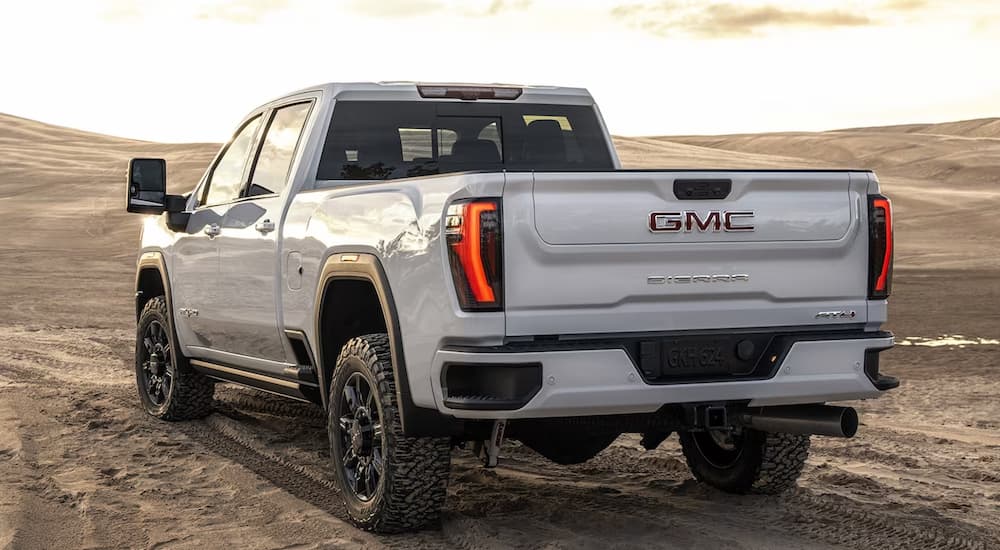 A white 2024 GMC Sierra HD AT4 is shown from a rear angle on a sandy desert area.