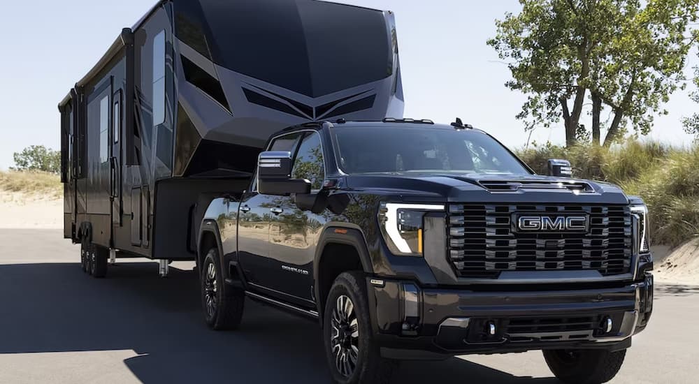 A black 2024 GMC Sierra 2500 HD Denali Ultimate is shown towing a camper trailer.