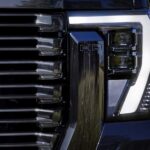 A close up of the headlight on a black 2024 GMC Sierra 2500 HD Denali Ultimate is shown.