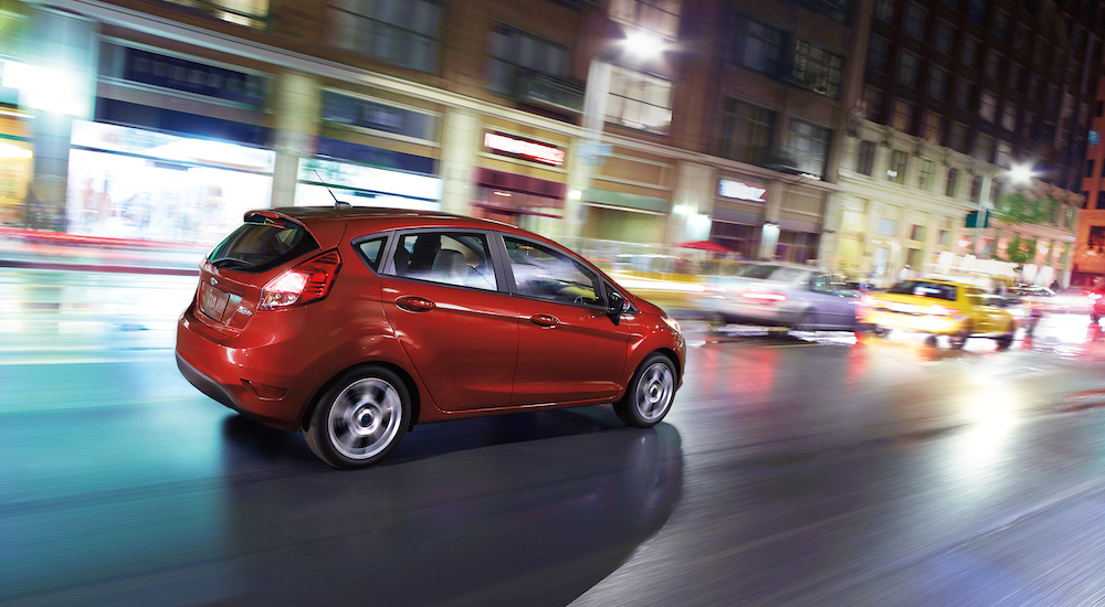 A red 2018 Ford Fiesta is shown from the side driving on a city street.