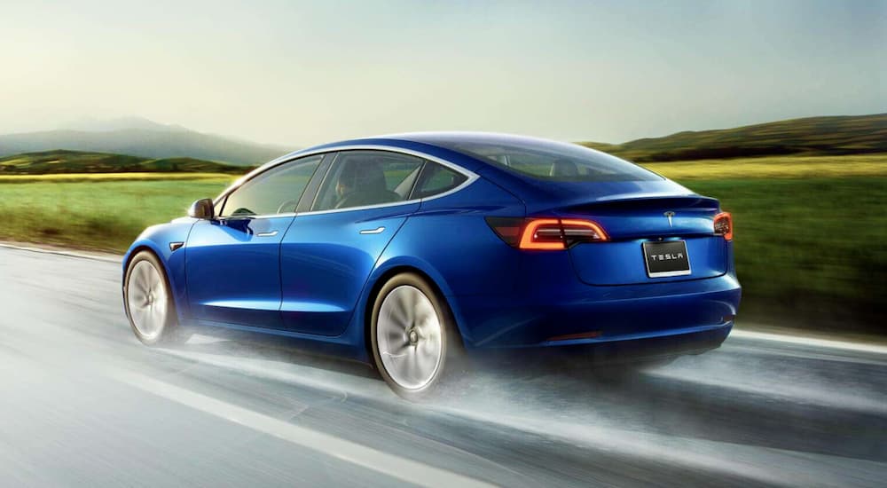 A blue 202 Tesla Model 3 is shown driving on a road.