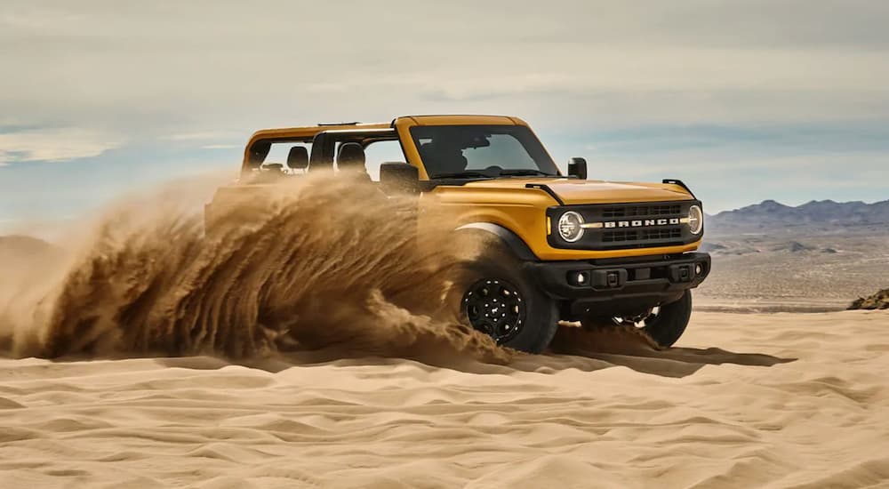 A yellow 2021 Ford Bronco is shown kicking up sand after leaving a Ford dealer.