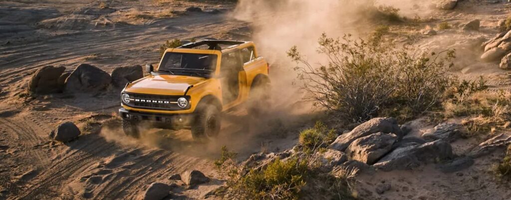 A yellow 2021 Ford Bronco is shown on a dusty trail.
