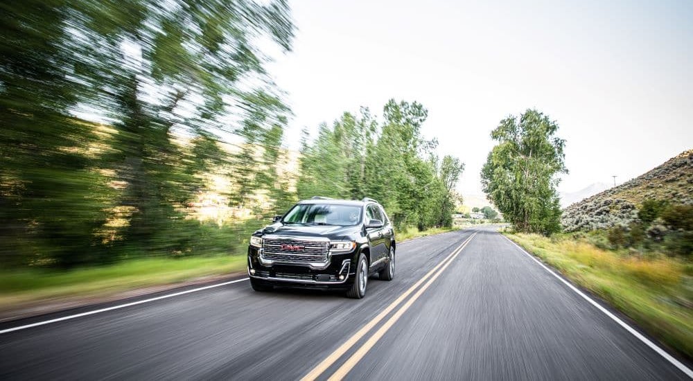 A black 2020 GMC Acadia Denali is shown driving past blurred trees.