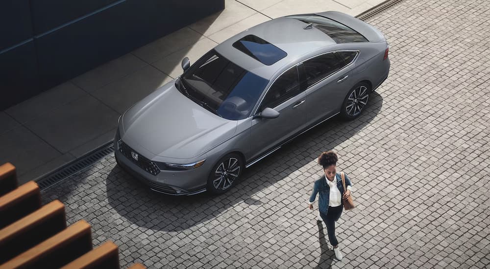 A person is shown walking away from a grey 2023 Honda Accord Touring on a city street.