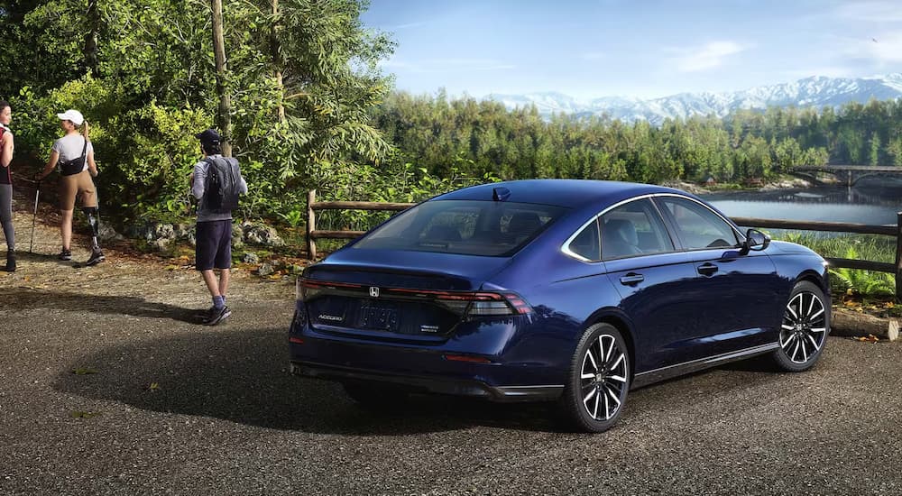 A blue 2023 Honda Accord Touring Hybrid is shown from a rear angle next to a hiking trail entrance.