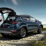 A blue 2020 Kia Sportage is shown as a man puts a surfboard in the rear cargo space.