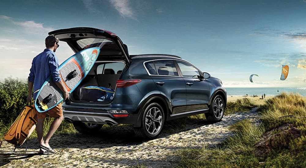 A blue 2020 Kia Sportage is shown as a man puts a surfboard in the rear cargo space.