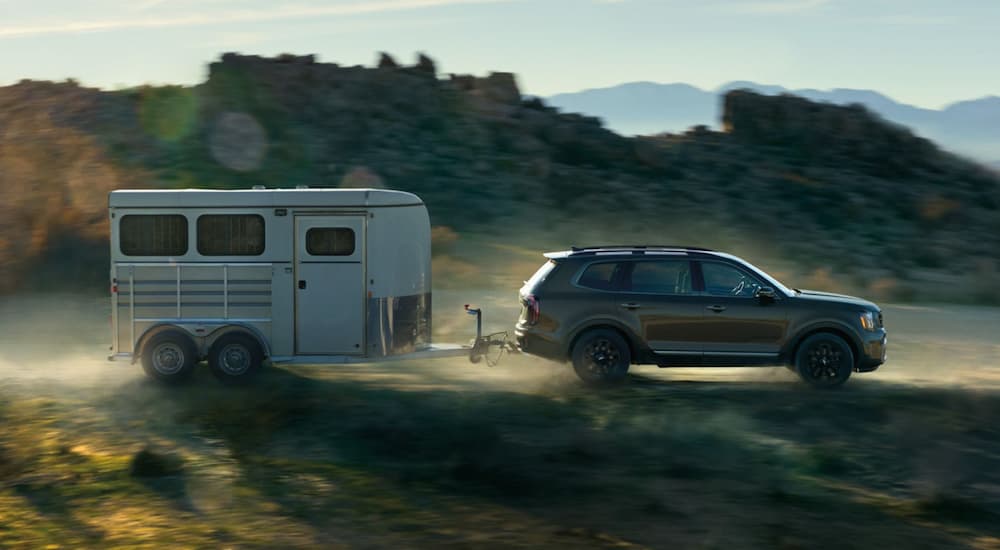 A black 2023 Kia Telluride X-Pro is shown from the side while towing a white enclosed trailer.