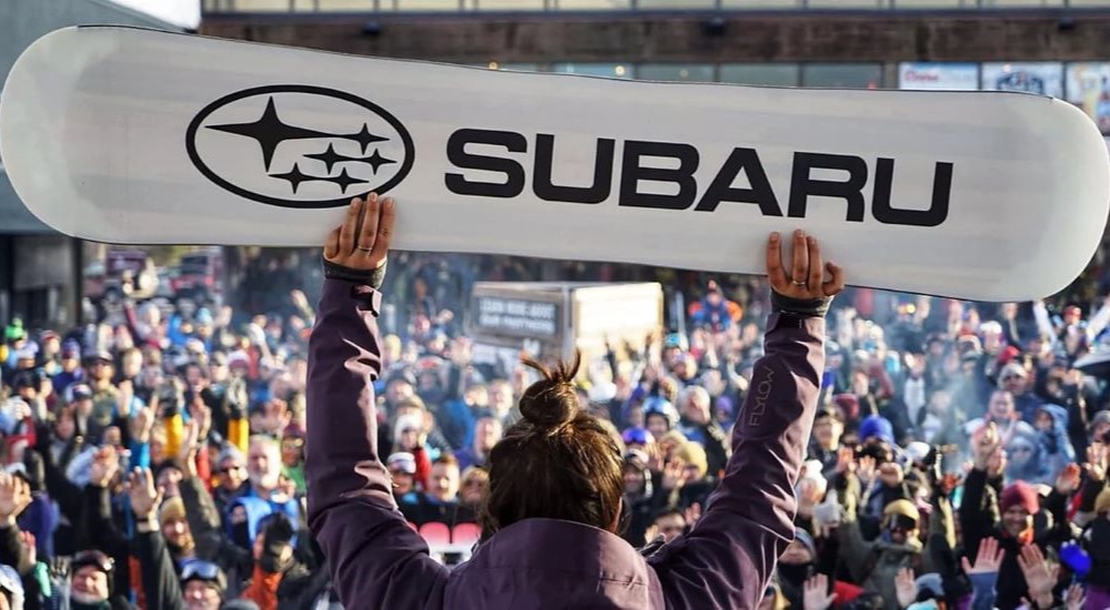 A close up shows the Subaru logo on a snowboard.