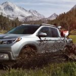 A silver 2020 Honda Ridgeline RTL-E is shown off-roading on a muddy trail.