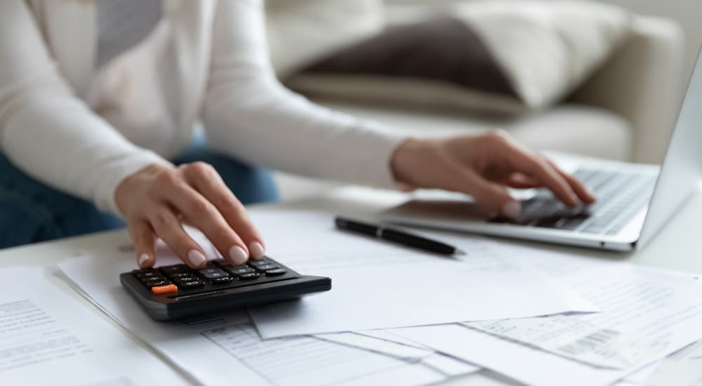 A person is shown using a calculator and laptop to do their taxes.