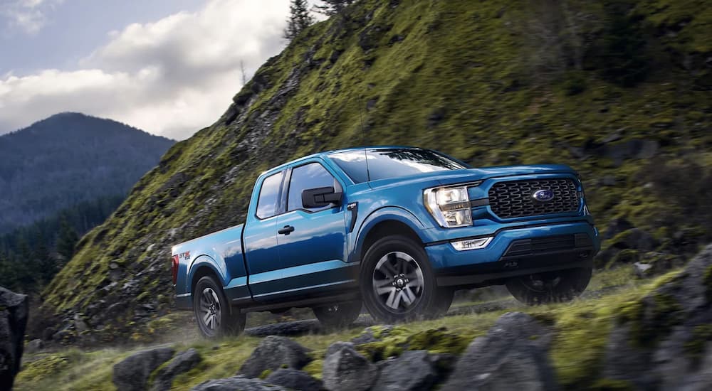 A blue 2021 Ford F-150 STX is shown driving on a mountain road after viewing used ford trucks near you.