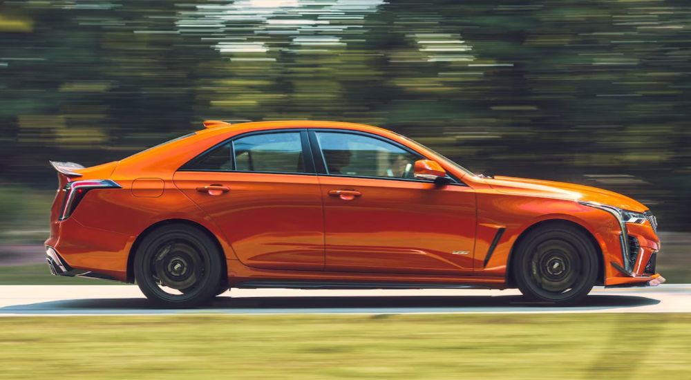 An orange 2023 Cadillac CT4 V-Series is shown speeding down a country road on a sunny day coming from a Cadillac dealer.