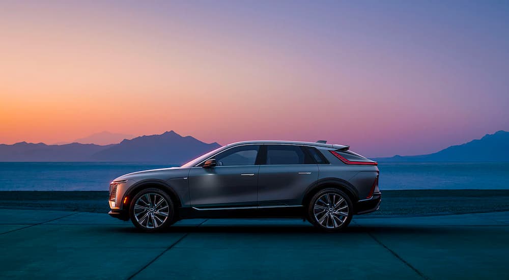 A 2023 Cadillac Lyriq is shown parked in front of a mountain range at sunset. 