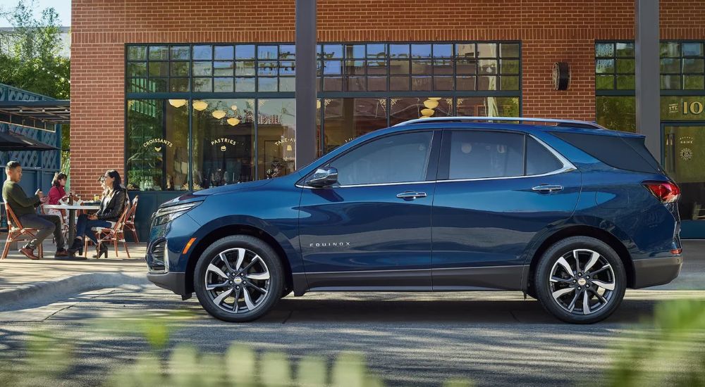 A blue 2023 Chevy Equinox is shown parked outside a cafe with people outside enjoying their coffee.