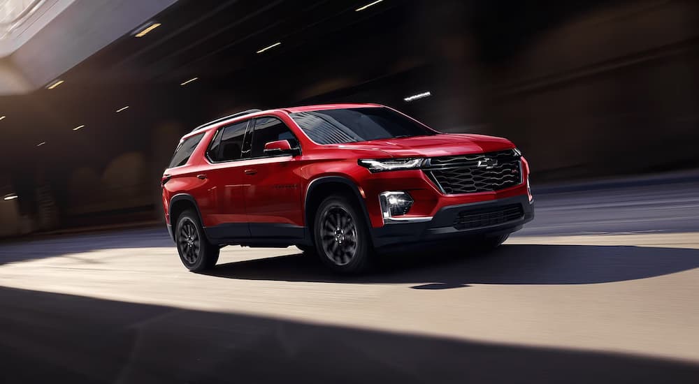 A red 2023 Chevy Traverse for sale is shown on a test drive on a city street.