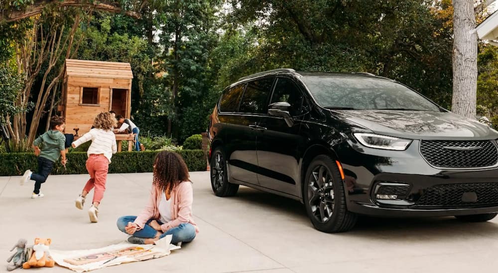 A mother and kids are shown playing next to a parked black 2023 Chrysler Pacifica