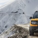 A yellow 2023 Ford Bronco Sport is shown driving along a trail on the side of a snowy mountain.