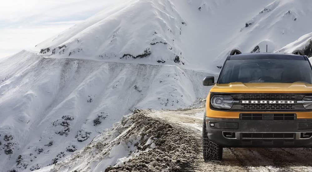 A yellow 2023 Ford Bronco Sport is shown driving along a trail on the side of a snowy mountain.