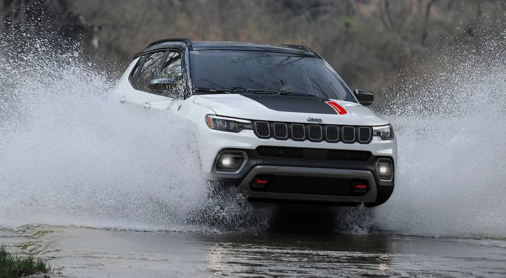 A white 2023 Jeep Compass Trailhawk is shown splashing through a river in a 2023 Ford Bronco Sport vs 2023 Jeep Compass comparison.