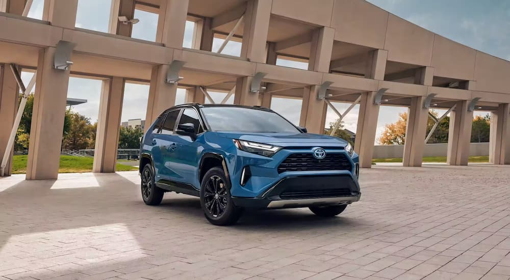 A blue 2023 Toyota RAV4 is shown parked in front of a modern structure.