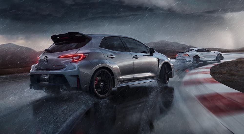 A 2023 silver Toyota GR Corolla is seen drifting behind a white Toyota GR Supra on a racetrack in the rain.