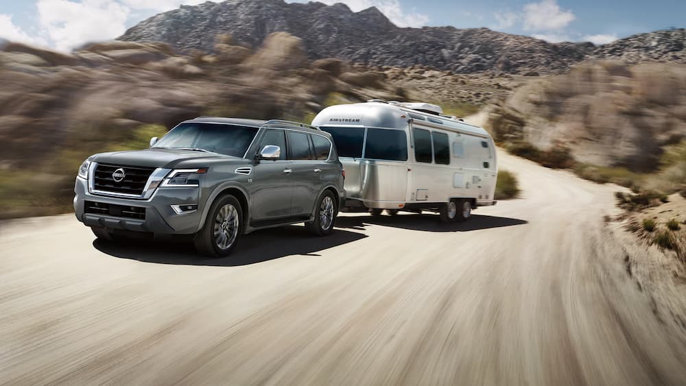 A gray 2023 Nissan Armada pulling a trailer up a dirt road.