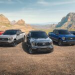 Five 2023 Ford F-150 trucks, the most popular model looking at car sales, in a variety of colors are shown lined up against an arid mountain backdrop.