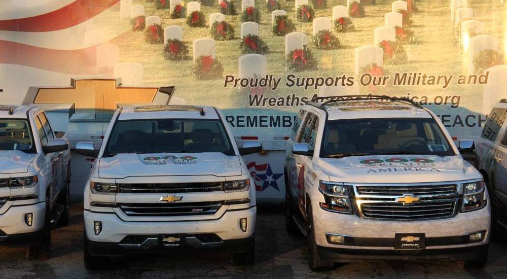 A white 2016 Chevy Silverado 1500 Z71 and a Chevy Suburban are shown in front of a mural.