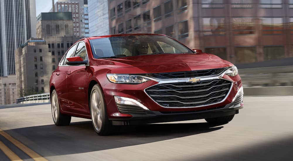 A red 2023 Chevy Malibu is shown driving through a city.