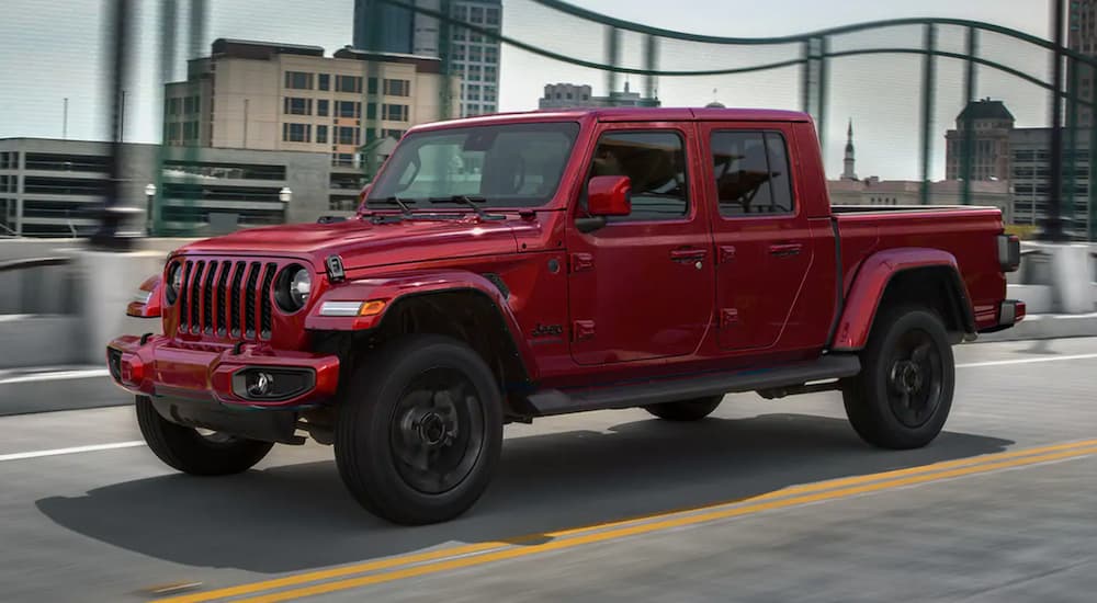 A red 2023 Jeep Gladiator for sale is shown driving on a city bridge.