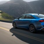 A blue 2023 Kia Forte for sale is shown driving.
