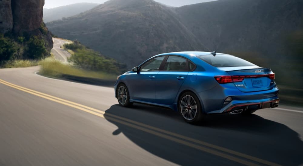 A blue 2023 Kia Forte for sale is shown driving.