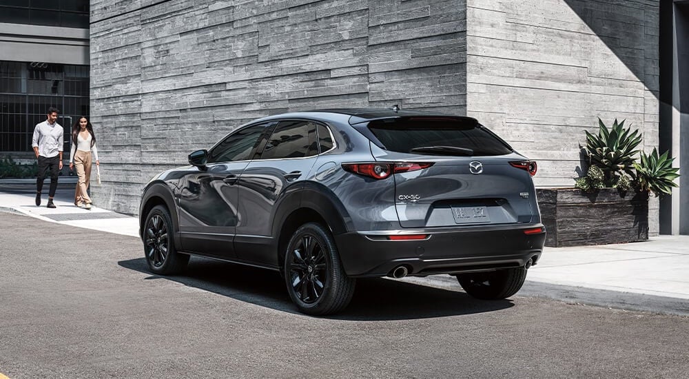 A man and a woman are shown walking up to a silver 2023 Mazda CX-30 for sale.