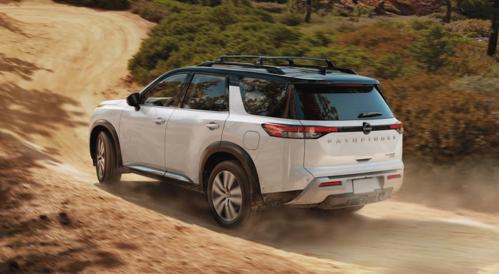 A white 2023 Nissan Pathfinder is shown driving up a dirt road away from a Nissan dealer.