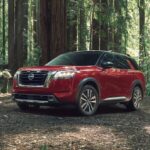 A red 2023 Nissan Pathfinder is shown parked in a forest.