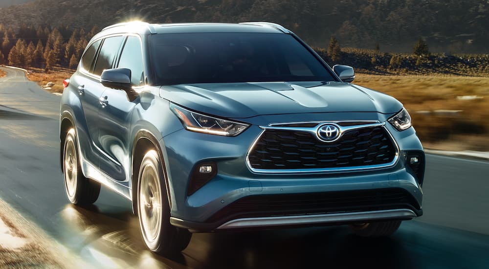 A blue 2023 Toyota Highlander is shown driving along a country road.